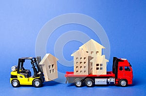 A yellow forklift loads a house figures on a red truck. Concept of transportation and cargo shipping, moving company. Construction