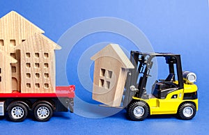 A yellow forklift loads a wooden figure of a house into a truck. Concept of transportation and cargo shipping, moving company