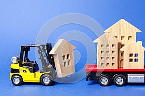 A yellow forklift loads a wooden figure of a house into a truck. Concept of transportation and cargo shipping, moving company