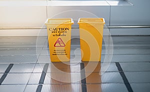 The yellow garbage bin and caution wet floor sign for the people . The Public trash on the side of the way to parking car in the