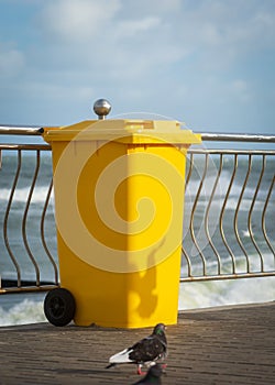 Yellow garbage container by the sea .