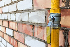 Yellow gas pipe with a crane goes along the facade of a old brick wall. House connected to gas for domestic use