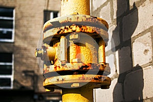 Yellow gas pipe with valve open close goes along the facade of a multi-storey building.