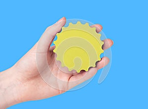 Yellow gear in hand over blue background. Person holding sun model over sky