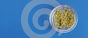 Yellow gelatin capsules with vitamin D3 in a glass container on a blue background. Pharmaceutical therapeutic and prophylactic