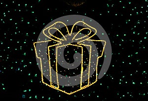 Yellow gift box with christmas lights and ribbon on blurred festive background with green fluorescent backdrops