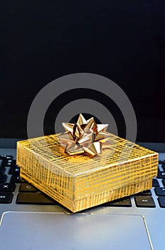 Yellow gift box sitting on a laptop computer keyboard close up