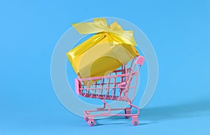 Yellow gift box with a silk bow in a miniature metal trolley on a light blue background