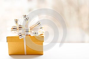 Yellow Gift box wrapped in white and gold striped ribbon on light background. Empty note tied over. copy space . place for text