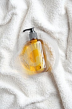 Yellow glass dispenser bottle with shower gel on white towel in bathroom