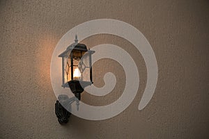 A yellow glass lantern hanging on a gray old wall. Bright glowing lantern illuminating the wall of an ancient building