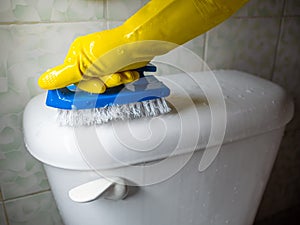 a yellow gloved hand cleaning a white toilet bowl with a blue hand brush