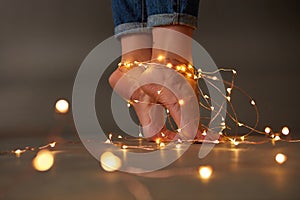 Yellow glowing garlands on the floor adorning girl`s legs around a dark background. Creative holiday composition