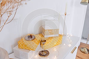 Yellow, gold gift boxes lie on a modern bedside table. The vase contains dried flowers, candlesticks