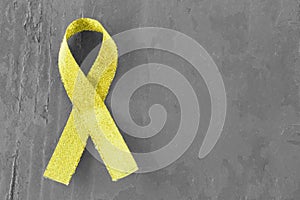 Yellow, gold ribbon on black and white wooden background, close-up, copy space, medical concept, Suicide Prevention Day