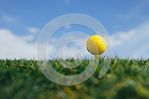 Yellow golf ball on tee, green grass and blue sky