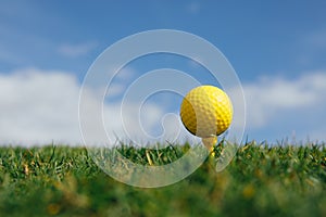 Yellow golf ball on tee, green grass and blue sky background