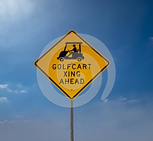 Yellow Golf Cart Crossing sign with black letters against a blue sky