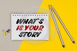 On a yellow-gray background are pencils, buttons and a notebook in which it is written - WHAT S IS YOUR STORY