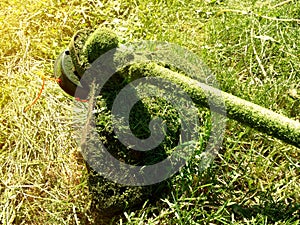 Yellow-green backdrop with electric  manual trimmer with orange braided wire fishing line in mowed grass