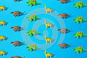 Yellow green Brachiosaurus, gray Ankylosaurus and green Stegosaurus dinosaur toy on a blue background. Pattern