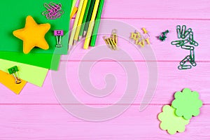 Yellow and green pencils, felt-tip pens, notepaper, paper clips, stationery nails, felt and smiles on pink wooden background