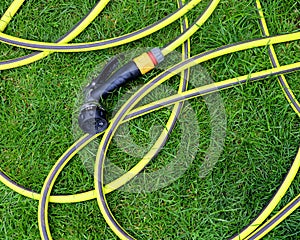 A yellow and green plastic hose pipe on green grass.