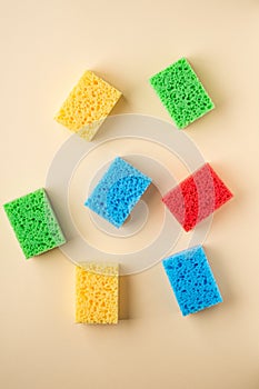 Yellow, green, red, blue sponges on cream colored paper background, copy space, top view, flat lay