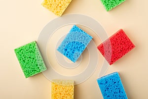 Yellow, green, red, blue sponges on cream colored paper background, copy space, top view, flat lay