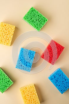 Yellow, green, red, blue sponges on cream colored paper background, copy space, top view, flat lay