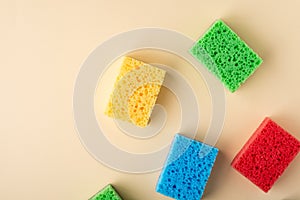 Yellow, green, red, blue sponges on cream colored paper background, copy space, top view, flat lay