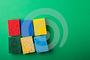 Yellow, green, red, blue sponges on green colored paper background, copy space, top view, flat lay