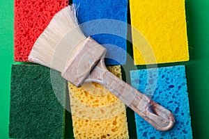 Yellow, green, red, blue sponges with paint brush on green colored paper background, copy space, top view, flat lay