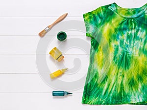 Yellow and green tie dye t-shirt on a wooden table with paint. Flat lay