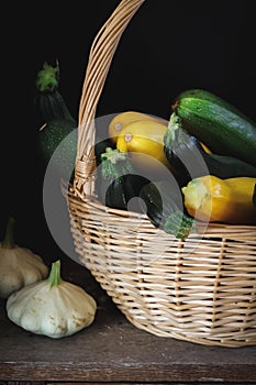 Yellow and green zucchini and button squash in a basket on a dark background, vertical