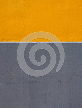 Yellow and grey areas of paint on a rough textured concrete wall divided by a horizontal white stripe