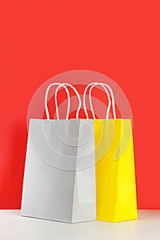 Yellow and grey shopping or gift bags on wooden desk against red background