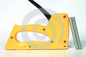 yellow gun tacker with staples, on white background and reflection