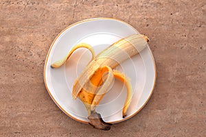 Yellow half peeled banana on brown concrete background. Still life with fresh organic fruit on the plate. Flat lay. Close up, top