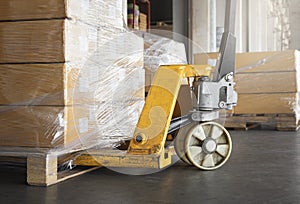 Yellow hand pallet truck with cardboard boxes stack on pallet rack. Storage warehouse.