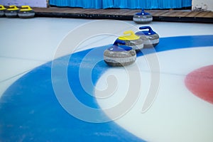 A yellow-handled stone stands between two blue-handled curling stones on the blue circle of the House