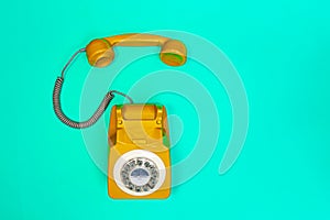 Yellow handset of a telephone on a green mint background.