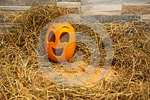 Yellow and happy smiling pumpkin. Halloween symbol on a gray stone wall background, stands on a hay and a wooden stand. Jack o