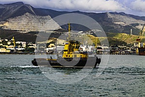 Yellow harbor tug close-up against the backdrop of the seaport and mountains.