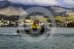 Yellow harbor tug close-up against the backdrop of the seaport and mountains.