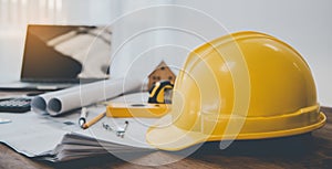 Yellow hard hat safety helmet placed on a work desk with a design plan of the house Including engineering equipment