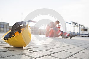 Yellow hardhat at shipyard with depressed male worker in background