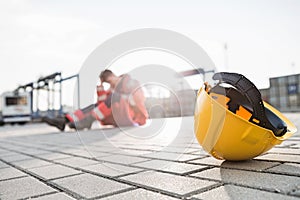 Yellow hardhat at shipyard with depressed male worker in background