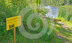 yellow Harmful algal bloom danger sign at small pond in Summer