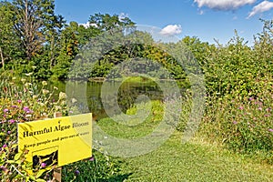 yellow Harmful algal bloom danger sign at small pond in Summer